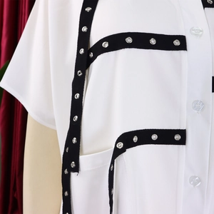 Detail of white short sleeve shirt featuring black straps and silver metal eyelets