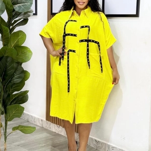 Detail of yellow oversize shirt dress featuring black straps with metal eyelets