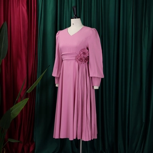 Detail of pink V-neck dress featuring 3D floral accent and pleated asymmetrical skirt