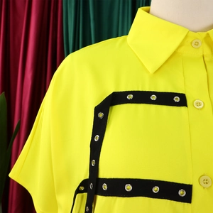 Detail view of yellow shirt collar with black trim and silver metal grommets