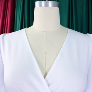 Close-up of deep V-neckline with cross-overlap and gathered texture on white dress