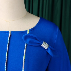 Detail of royal blue dress with round neck and green gingham bow decoration on mannequin