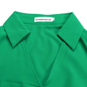 Close-up of the V-neck collar and stitching detail on a pleated emerald green dress