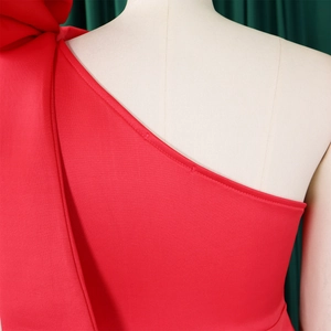 Detail of red one-shoulder dress showing oversized bow and neat stitching on smooth fabric