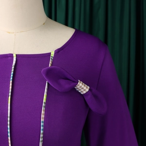 Detail of purple square neck dress with bow decoration and checkered edge piping