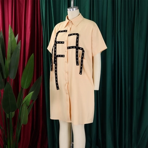Detail of light apricot shirt dress featuring black strap decor and silver eyelet accents