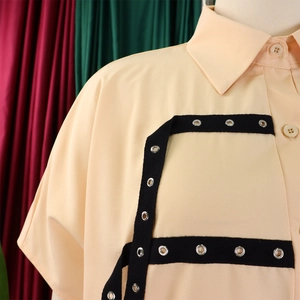 Detail of light peach short sleeve shirt featuring black straps and silver metal eyelets