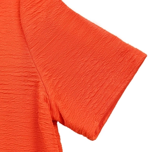 Gros plan sur la texture du tissu seersucker orange vif de cet ensemble pour femme