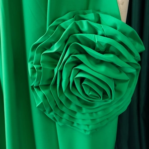 Detailed close-up of handmade 3D satin rose applique on a grass green evening dress