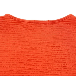 Gros plan du tissu orange gaufré montrant le col rond et les détails de couture