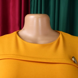 Dettaglio del vestito giallo zenzero con girocollo e bottone dorato decorativo sulla spalla