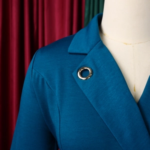 Détail du blazer bleu canard avec revers cranté et boucle décorative en métal doré