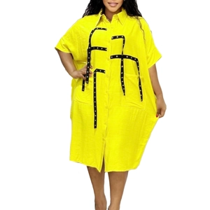 Detail of yellow loose shirt dress featuring black decorative straps with metal rivets