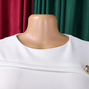 Dettaglio di un abito bianco a girocollo con bottone decorativo in metallo dorato