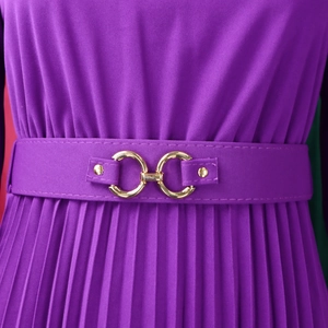 Dettaglio di un abito a pieghe viola con cintura sottile e fibbia dorata a doppio anello