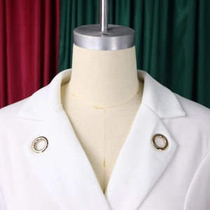 Vue détaillée du blazer blanc avec œillets métalliques dorés sur les revers et tissu chic