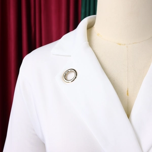 Détail d'une broche ronde dorée minimaliste sur le revers d'un tailleur blanc chic