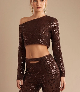 Dettaglio di paillettes marroni sul crop top monospalla a maniche lunghe e pantaloni