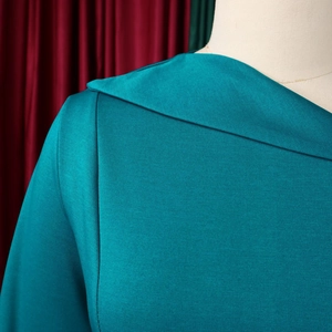 Close-up of teal dress fabric showing fine texture and neat neckline stitching detail