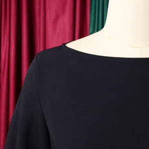 Dettaglio dell'elegante scollo a barchetta e della trama plissettata opaca sull'abito nero