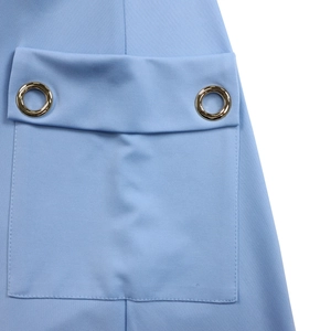 Détail d'une robe bleu clair montrant une poche à rabat avec des œillets métalliques