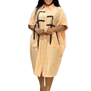Detail of loose apricot shirt dress with black webbed straps and metal eyelet accents