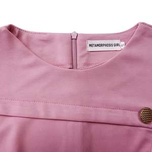 Dettaglio dello scollo rosa con etichetta METAMORPHOSIS GIRLS e bottone dorato