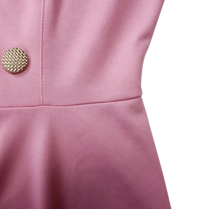 Dettaglio della vita di un abito rosa con cuciture rifinite e bottone dorato intrecciato