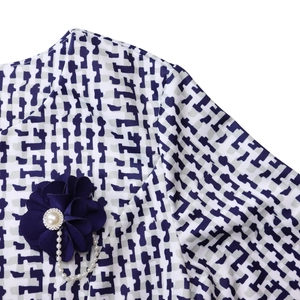 Détail de l'encolure à motif géométrique avec fleur en tissu et chaîne de perles