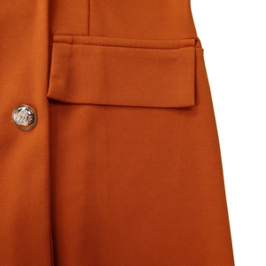Detailed macro view of orange blazer fabric with embossed silver metal button and flap pocket