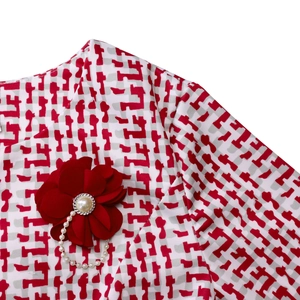 Détail de l'encolure avec broche fleurie rouge, perles et motifs géométriques