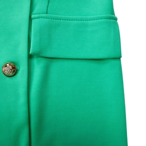 Macro detail of vibrant green blazer dress featuring a gold embossed button and flap pocket