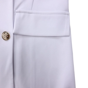Detailed close-up of a white blazer pocket with an ornate gold button and clean stitching
