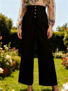 Detail of high waisted black wide leg trousers with decorative buttons in a garden setting