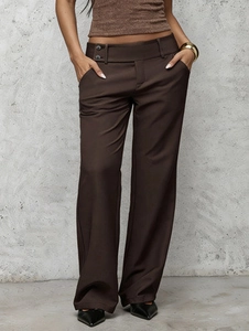 Detail view of high waisted brown trousers with side buttons and pockets on the waistline