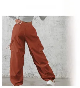 Detail of high-waisted cargo pants with large side pockets and drawstring cuffs in rust red