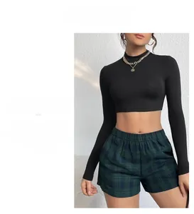 Dettaglio del crop top a maniche lunghe con collo alto, catena d'oro e shorts a quadri