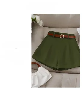 Detail of high-waisted olive shorts with brown leather belt on a neutral sofa