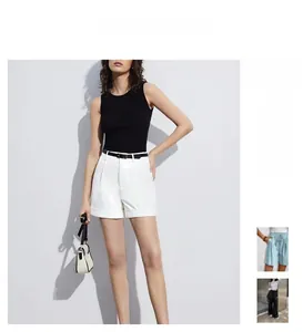 Detail of high-waisted white pleated shorts paired with a slim black top and belt