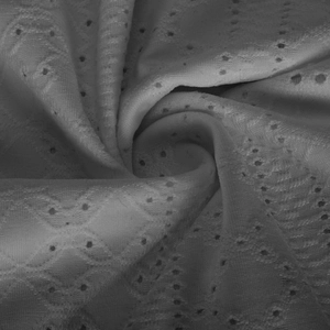 Detailed macro view of white eyelet embroidery fabric with intricate geometric floral lace