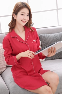 Detail of red silk pajama shirt with white piping and pocket embroidery on a sofa