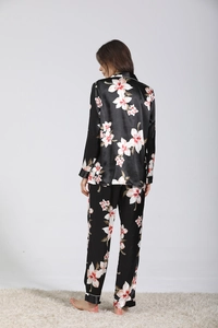 Vista posteriore di un set pigiama in raso nero da donna con fiori rosa e bordi bianchi
