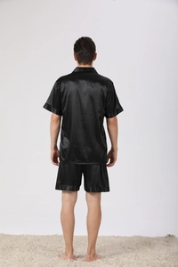Rear view of men's black satin pajama set with short sleeve top and shorts on white carpet