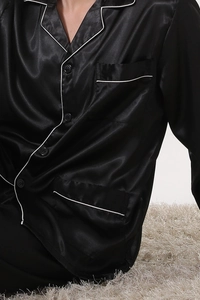 Detail of men's black satin pajama top featuring white contrast piping and smooth silk texture