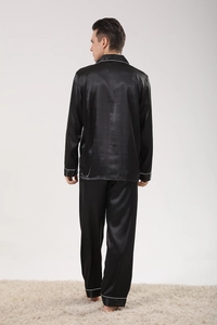 Rear view of black satin men's pajama set showing draping fit and white piping detail