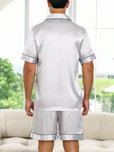 Rear view of men's silver grey satin pajama set with black trim in a bright home setting