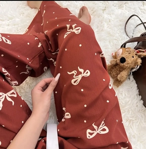 Detail view of brick red pajama pants with white bow prints on soft white plush carpet