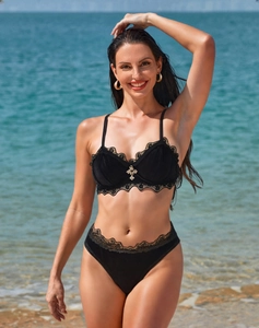 Dettaglio del reggiseno in velluto nero con pizzo e ciondolo a croce dorata sulla spiaggia