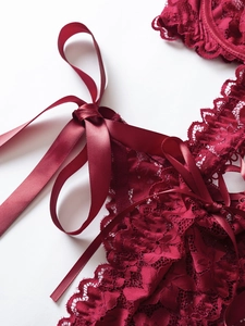 Detailed close-up of dark red floral lace texture and silky satin ribbon bow details