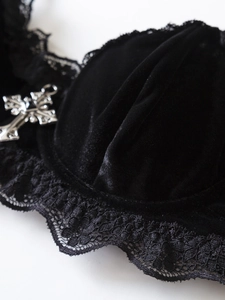 Dettaglio reggiseno in velluto nero con pizzo floreale e ciondolo a croce gotica